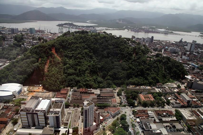 morro ao fundo com marca de escorregamento de encosta. prédios em primeiro plano e o mar ao fundo. #paratodosverem