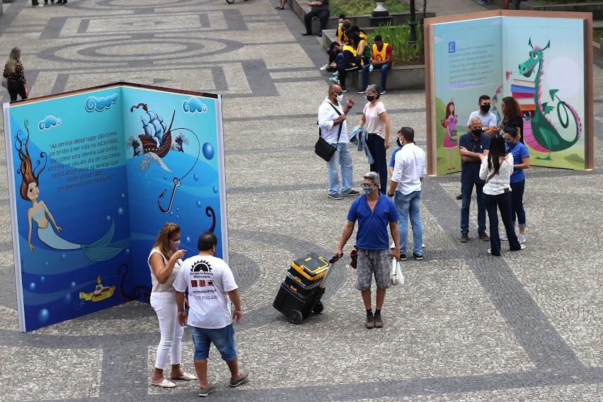 Grandes estruturas em formato de livros montadas na praça. Há pessoas circulando