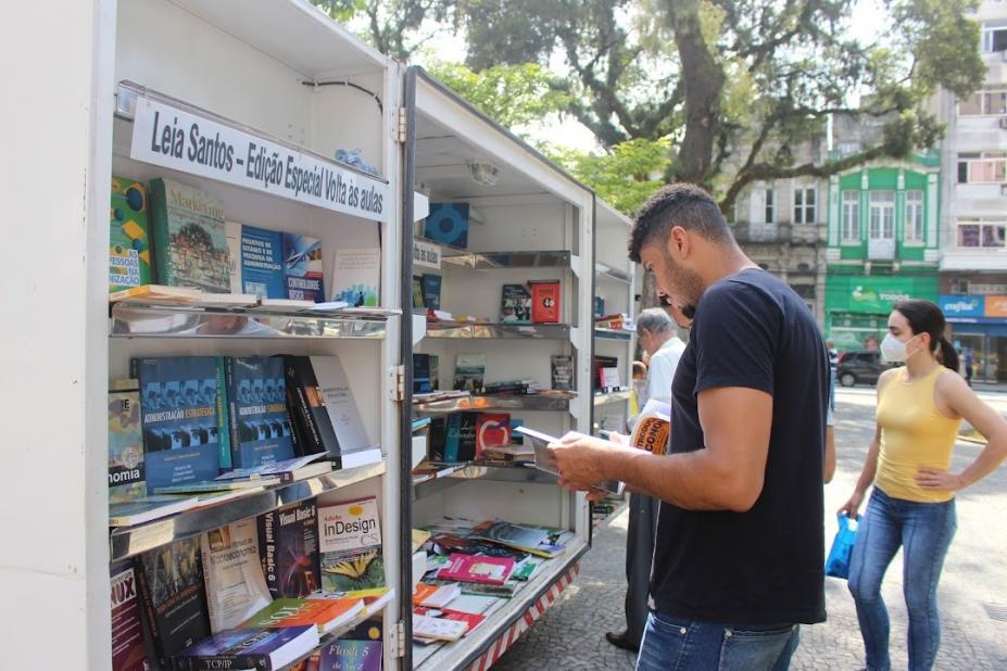 Homem escolhe livro na biblioteca móvel na Praça Mauá. #paratodosverem