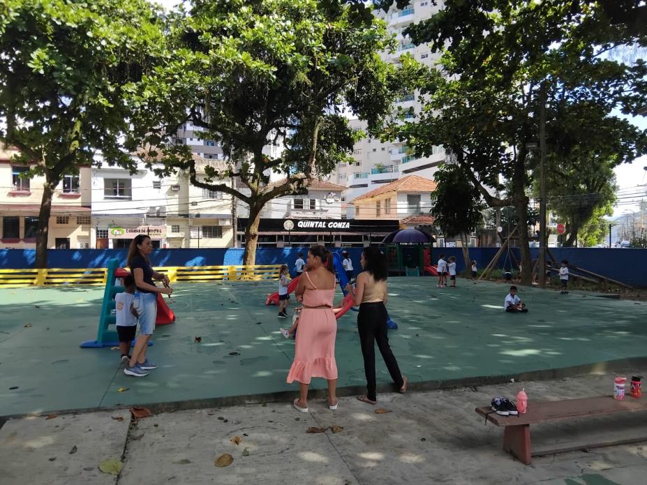 pessoas estão em parque infantil com piso recém-pintado de verde. #paratodosverem