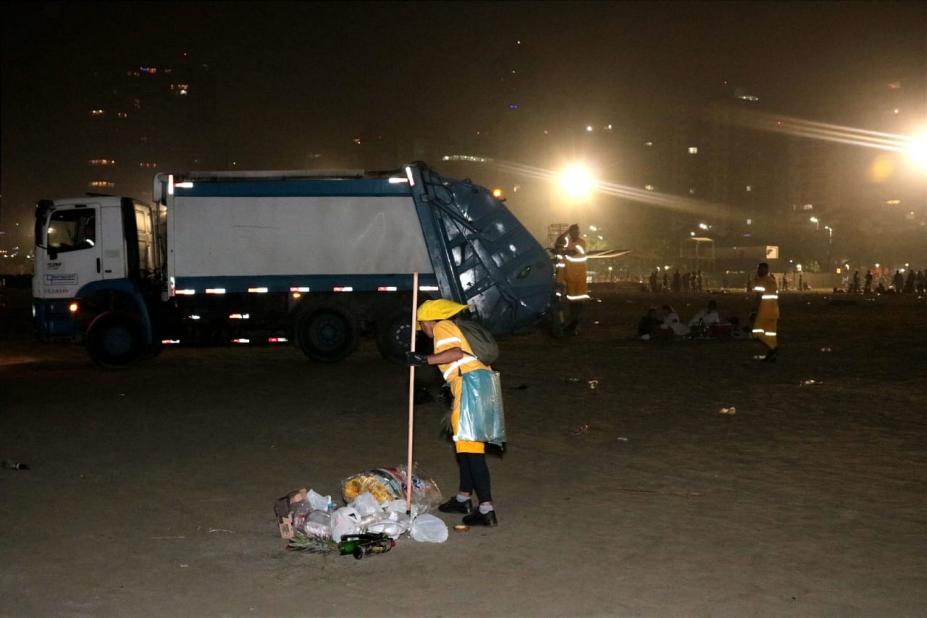 Profissionais de limpeza recolhem lixo na faixa de areia. #paratodosverem