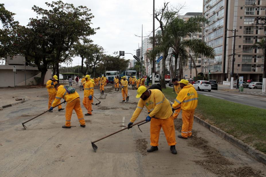 homens uniformizados varrem areia de avenida da orla. #paratodosverem