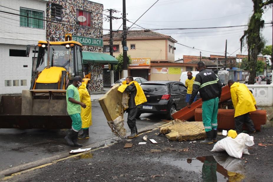 funcionários recolhem colchão e móveis em área próximo a um canal. #paratodosverem
