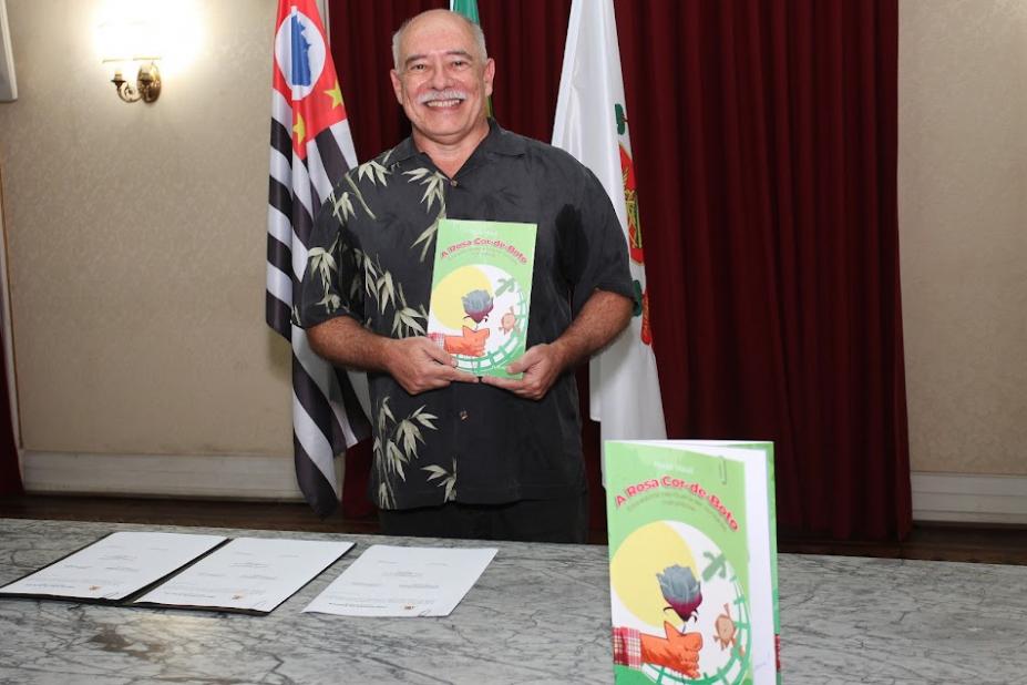 Escritor posa para foto segurando um exemplar do livro.#paratodosverem