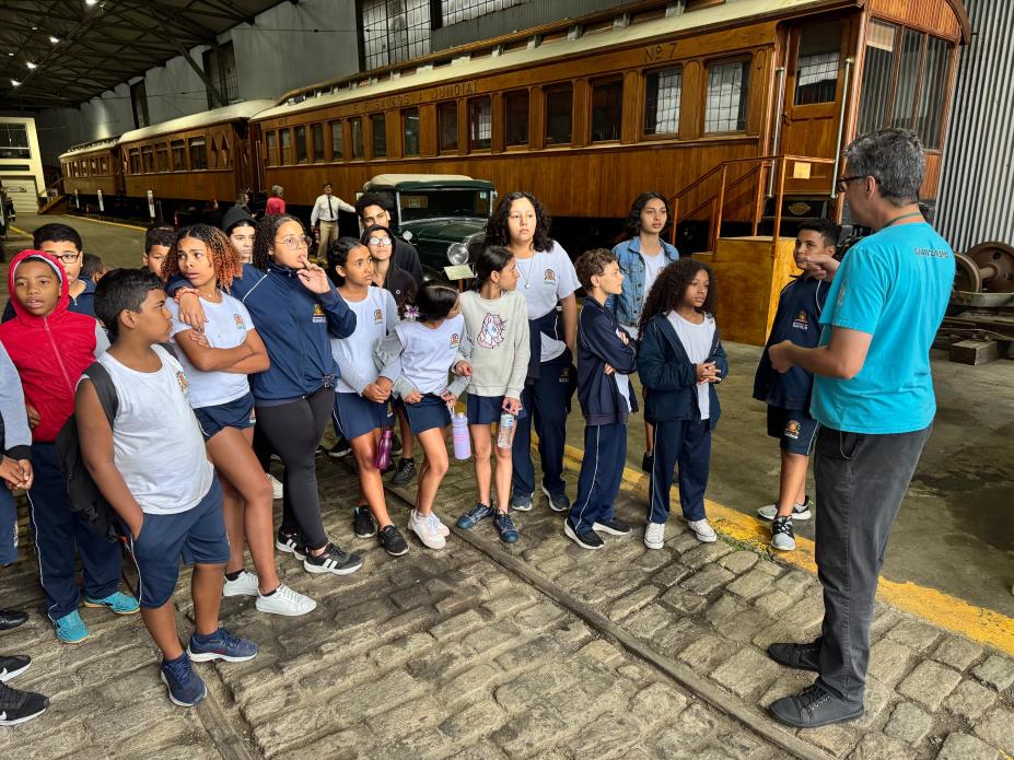 alunos ouvindo uma pessoa em pé #paratodosverem