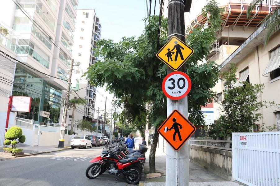 poste com três placas. Uma indica trânsito de crianças, outra a velocidade em 30 km/h e mais uma, indicando a presença de homens trabalhando. #paratodosverem