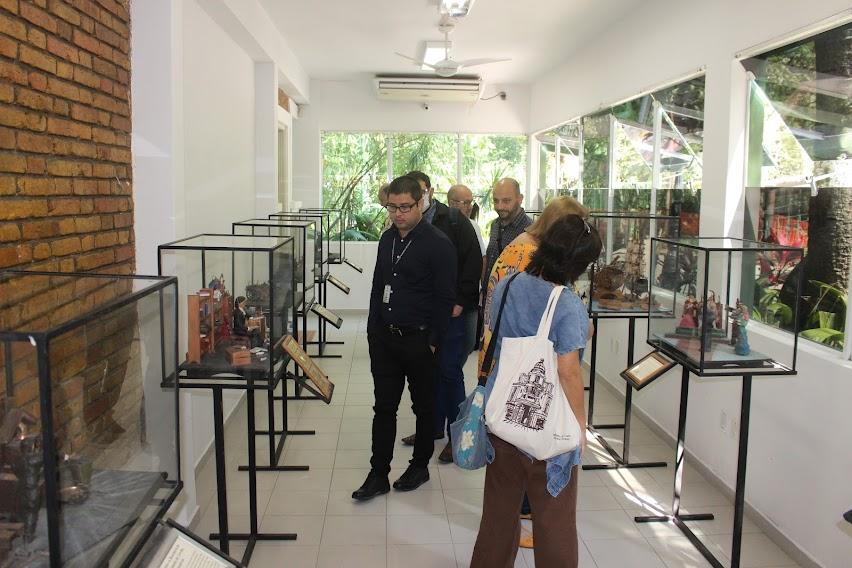 visitantes dentro de sala observando caixas de vidro onde estão as maquetes. #paratodosverem