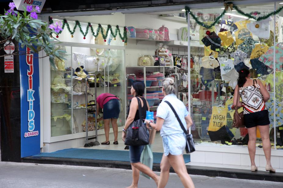 Pessoas caminham em frente a uma loja decorada para o Natal. 