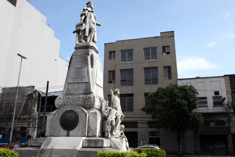 fachada do prédio com estátua e praça em primeiro plano #pracegover 