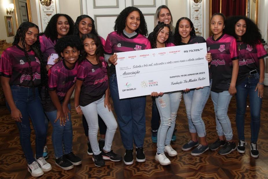 meninas posam para foto segurando cartaz que simboliza um cheque. #paratodosverem 