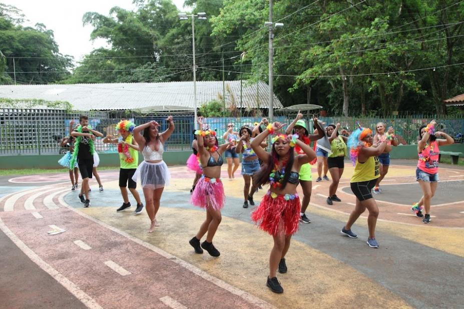 mulheres com roupas coloridas e fantasias dançam em uma quadra. #paratodosverem