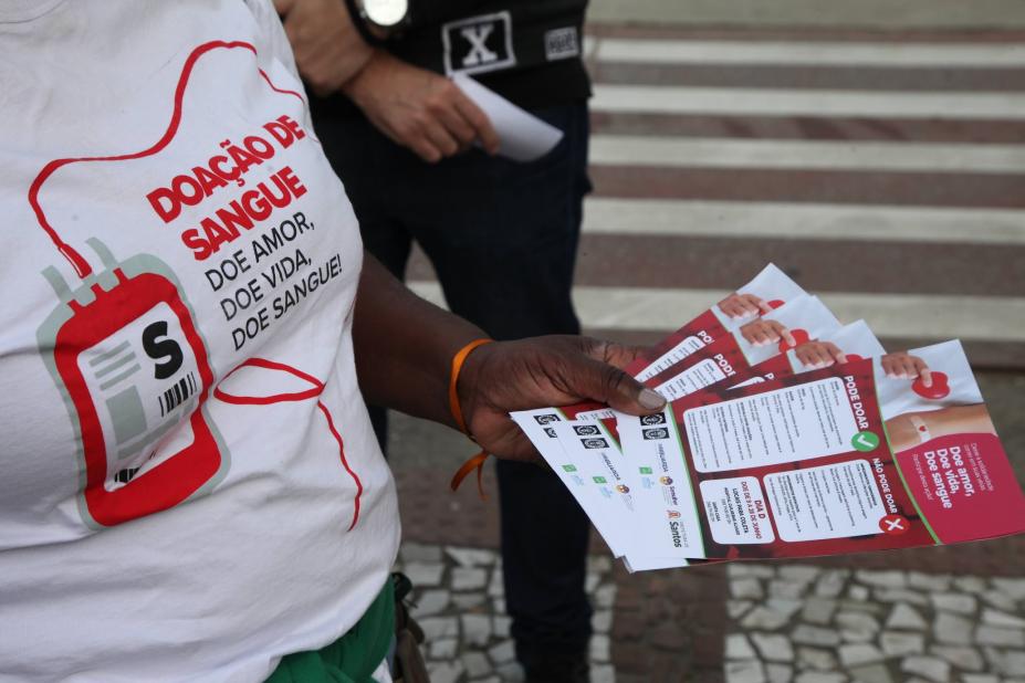 pessoa com camiseta da campanha segura folhetos educativos. #paratodosverem