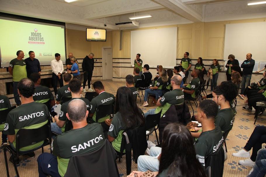 Atletas estão sentados em auditório. #paratodosverem