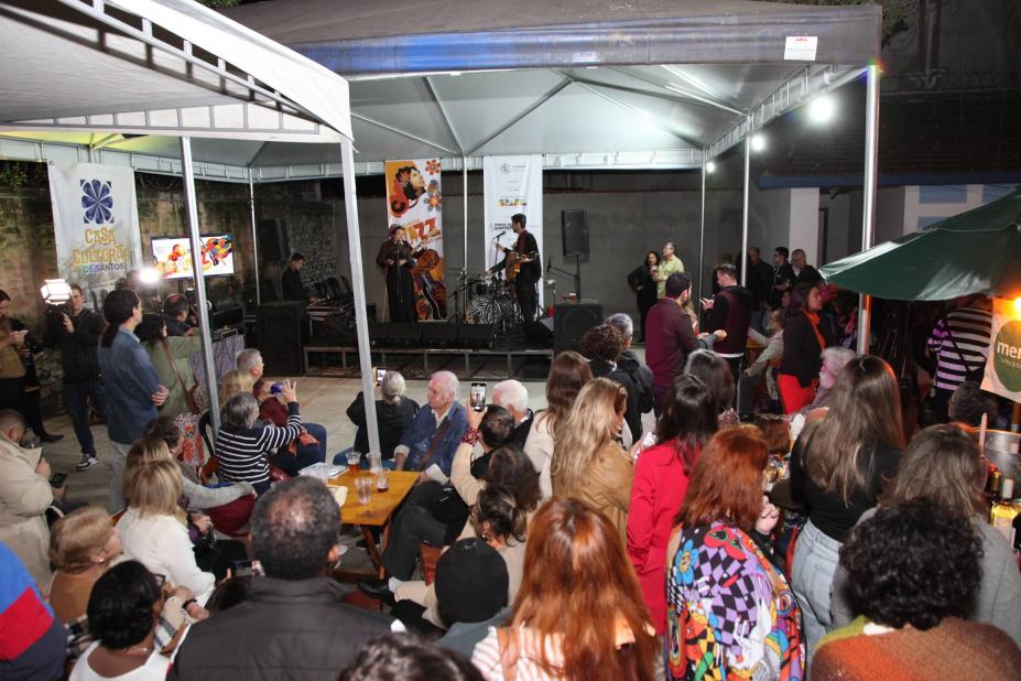 músicos cantam em palco com plateia ao fundo. #paratodosverem