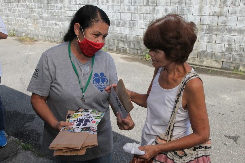 mulher usando máscara entrega folheto e saquinho de papel