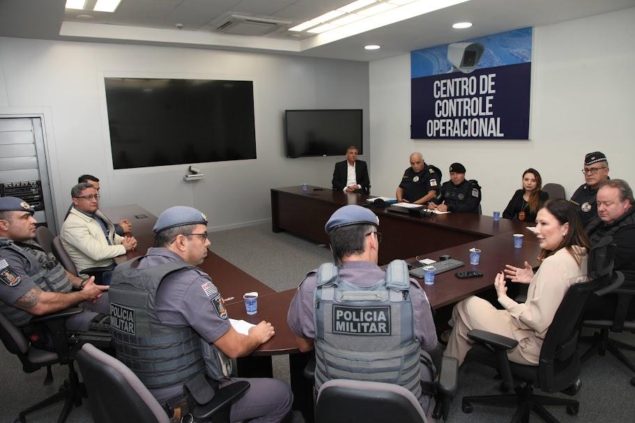 reunião com pessoas sentadas e conversando. Em primeiro plano, dois policiais militares identificados por coletes. #paratodosverem 