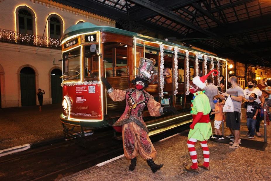 duendes estão diante de bonde decorado e iluminado. #paratodosverem