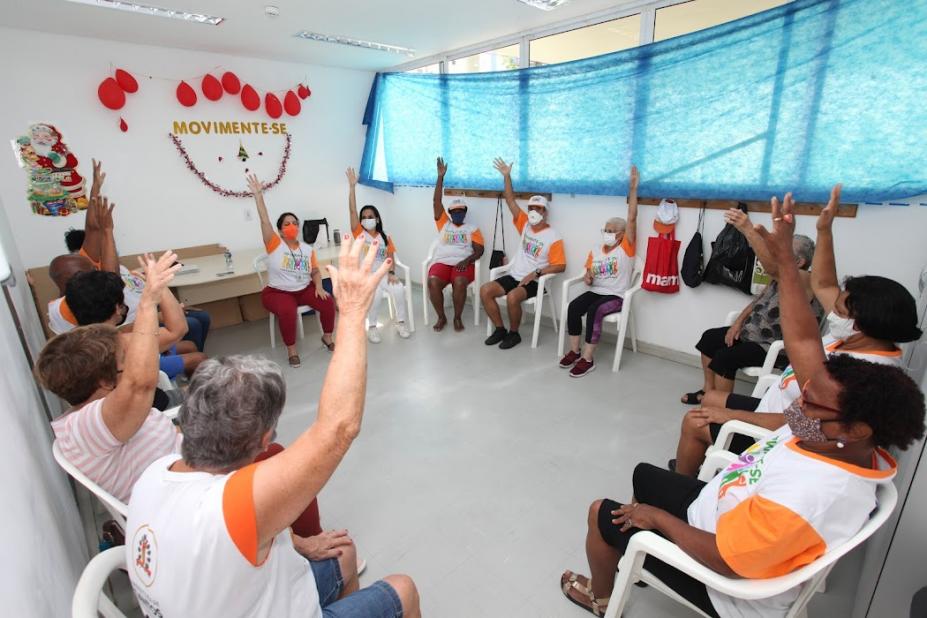 idosos sentados em circulo levantam a mão #paratodosverem