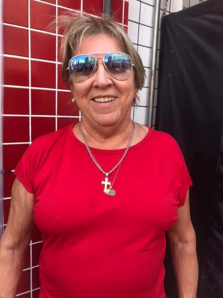 Maria Luiza, de blusa vermelha e óculos escuros, sorri para a foto. #pracegover