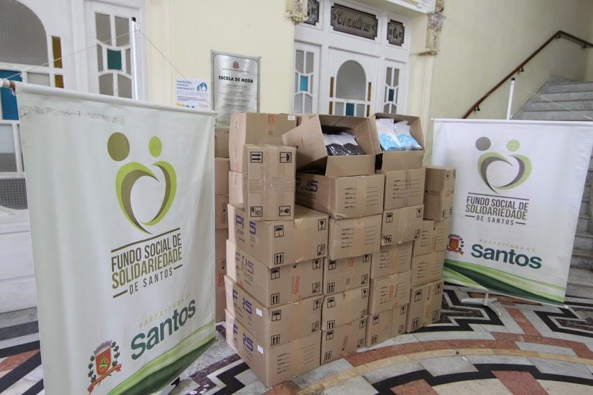 várias caixas de papelão empilhadas em uma sala e ladeadas por banners do Fundo Social de Solidariedade. #paratodosverem