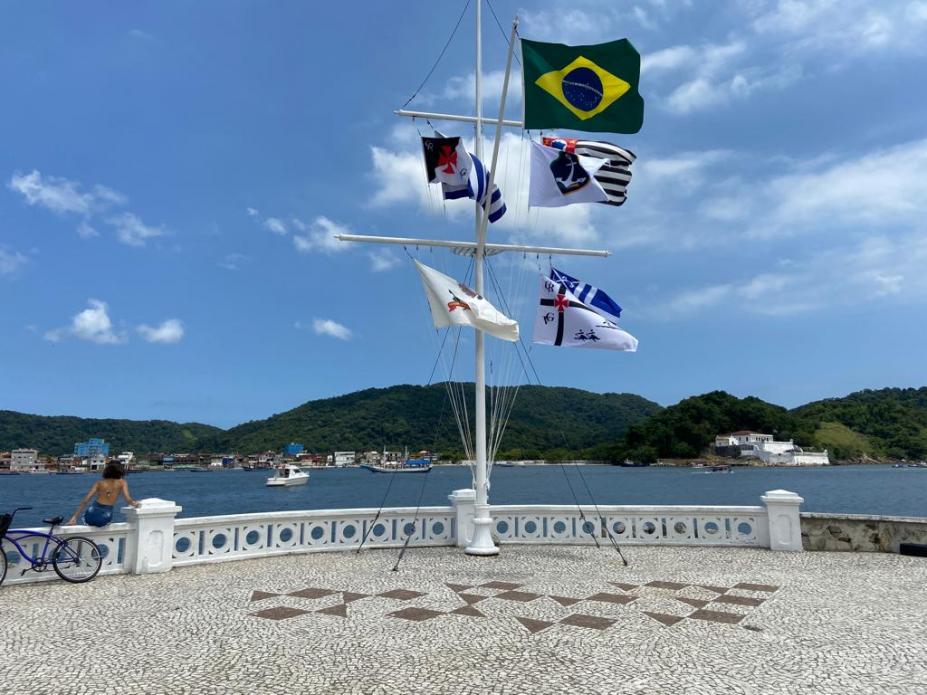 mastro com oito bandeiras de frente para o mar. #paratodosverem
