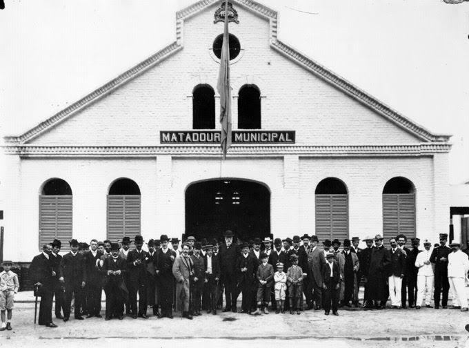 Fachada do Matadouro Municipal, com homens e crianças em frente. #pracegover