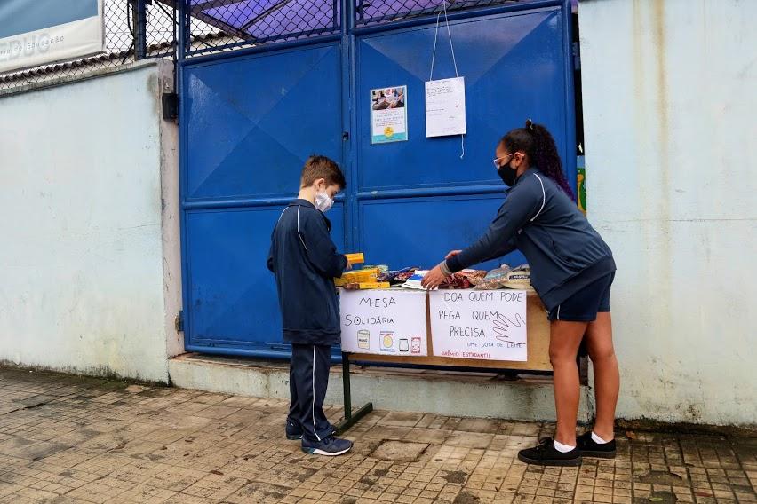 dois alunos estão arrumando pacotes de alimentos sobre uma mesa. #paratodosverem