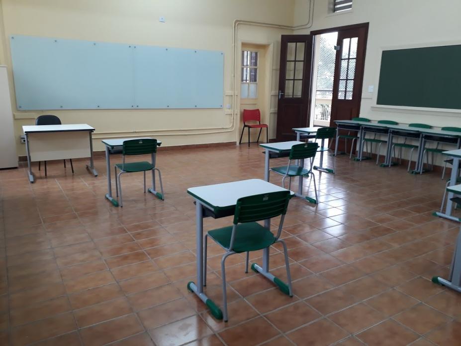 Mesas e cadeiras em sala de aula dispostas com longa distância entre umas e outras. #Paratodosverem