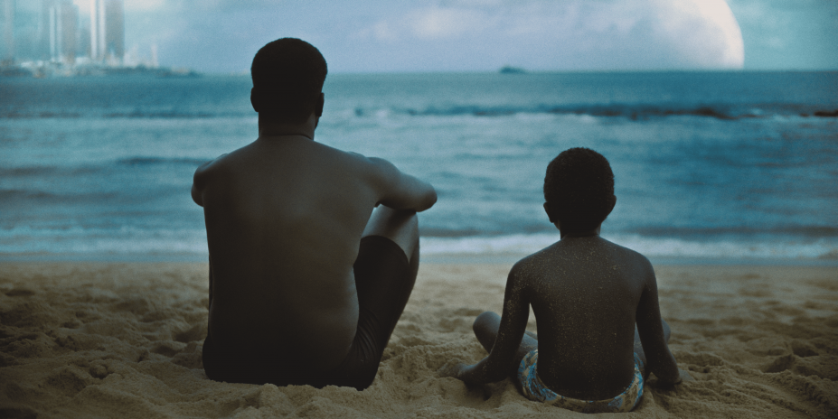 pai e filho olham para o mar em cena de filme #paratodosverem