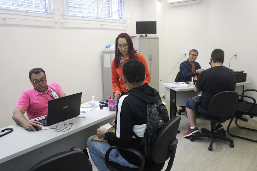 duas pessoas estão sentadas à mesa atrás de notebooks. Elas atendem munícipes. Trata-se do serviço do centro de emprego. O ambiente é uma sala de escritório. #paratodosverem