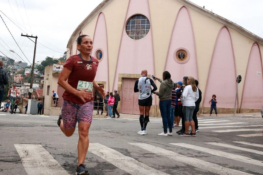 mulher corre e passa sobre faixa de pedestres. Ao fundo, uma igreja. #paratodosverem