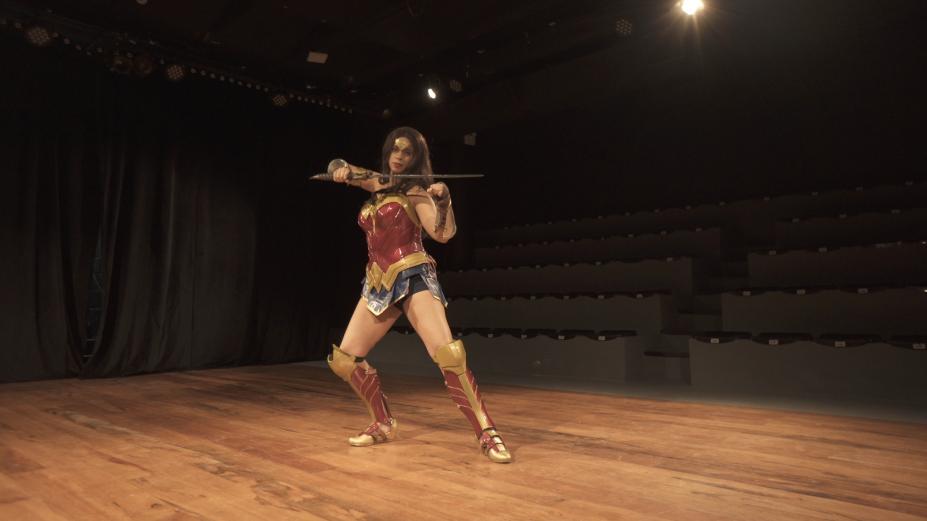 Menina está vestida de mulher-maravilha e faz pose empalco. #paratodosverem