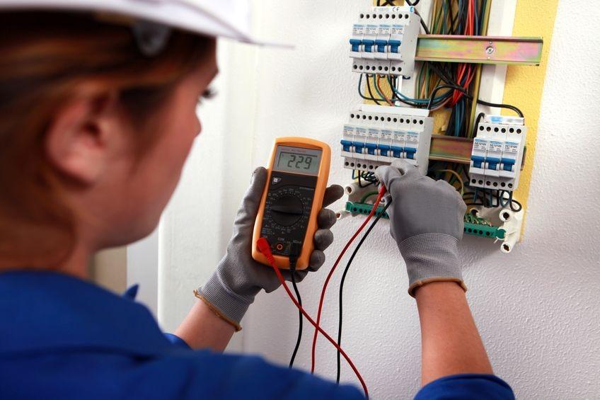 mulher está de costas mexendo em painel de lux. Ela segura um medidor de energia. #paratodosverem