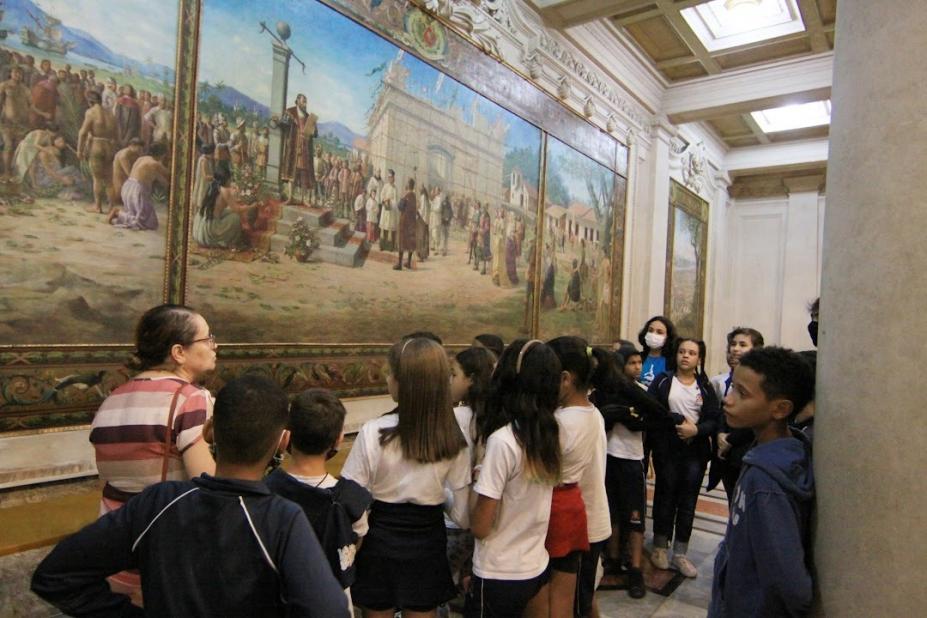 Crianças observam quadro no Museu do Café que retrata a fundação da Vila de Santos. #paratodosverem