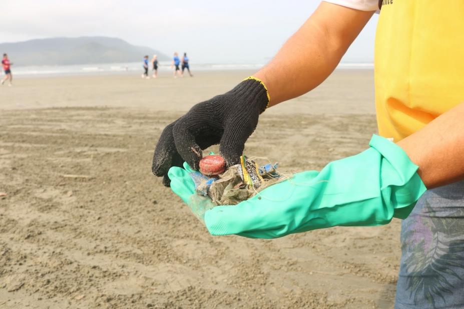 close de mãos com luvas segurando microlixos na faixa de areia da praia. #paratodosverem 