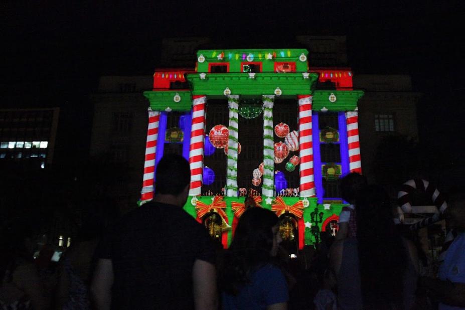 pessoas assistindo a projeção mapeada #paratodosverem