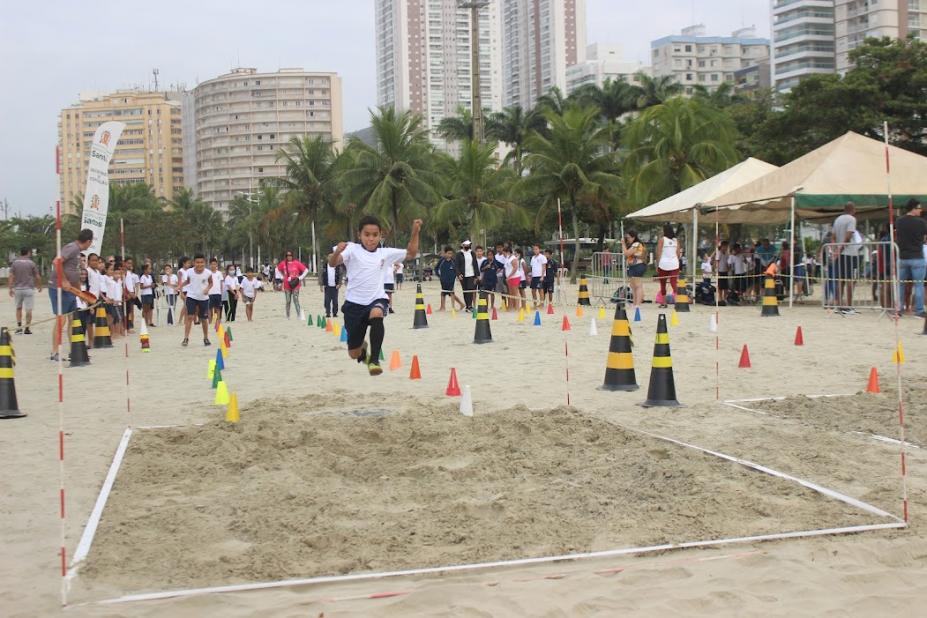 criança saltando na areia e várias assistindo ao fundo na praia #paratodosverem