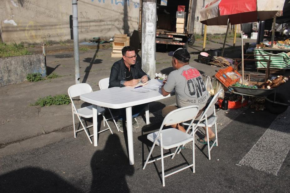 Em uma mesa na rua, homem recebe atendimento #paratodosverem