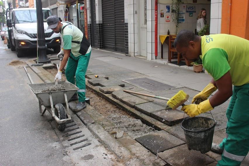 homens estão aplicando concreto em meio fio, ao lado de grelhas. #paratodosverem