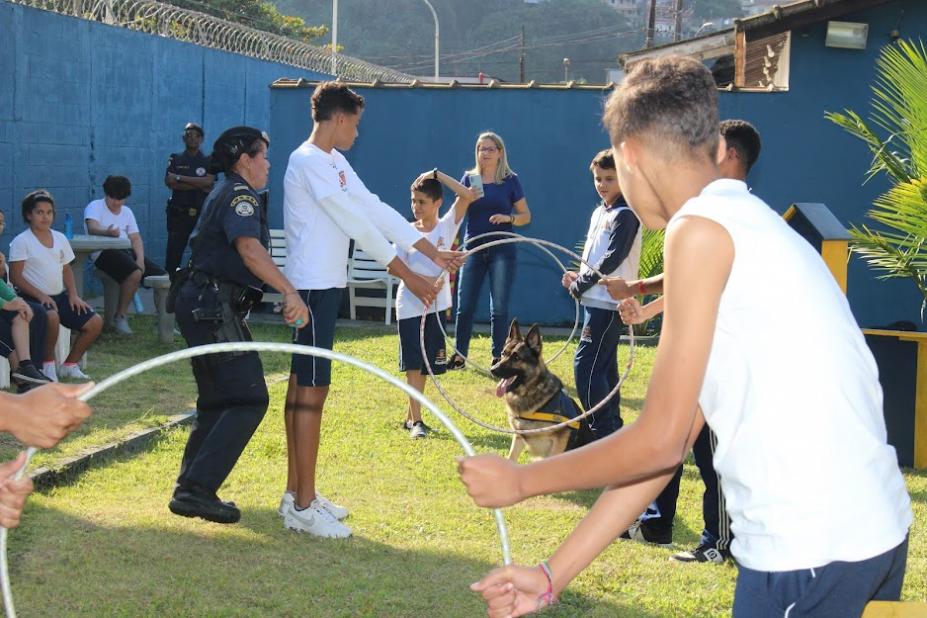 crianças seguram bambolês para cachorro passar entre eles. #paratodosverem