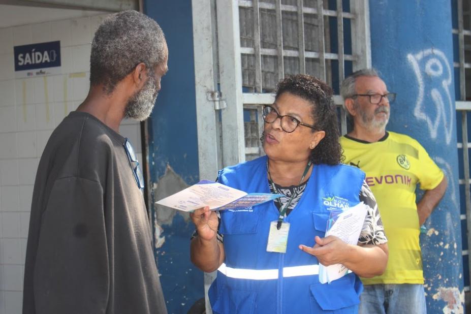 mulher entrega folheto para homem. #paratodosverem