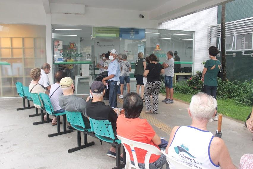 idosos sentados e em pé em porta de policlínica aguardando a vacinação. #paratodosverem