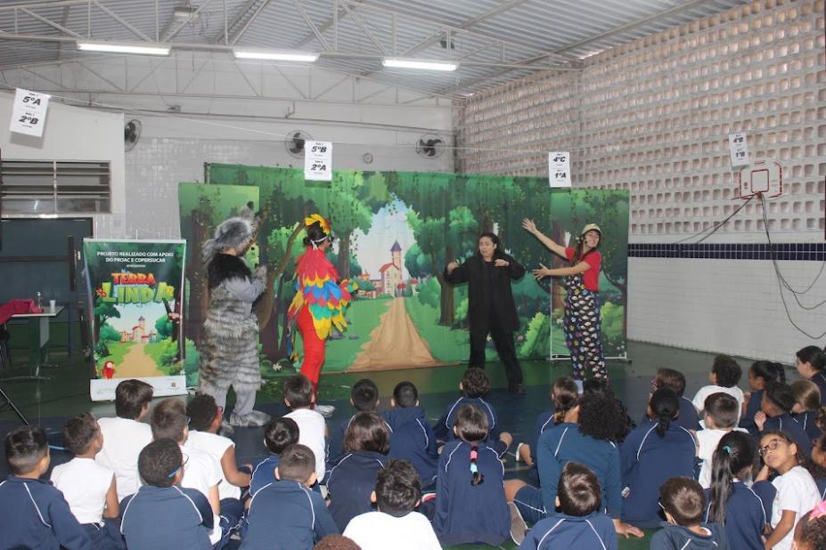 artistas estão no palco vestidos de animais. Crianças estão sentadas assistindo. #paratodosverem