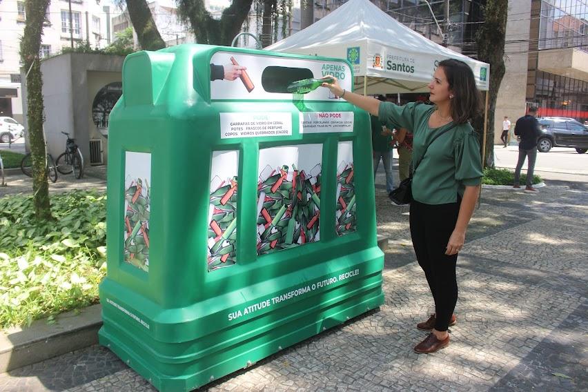 mulher coloca garrafa de vidro dentro de recipiente em praça. #paratodosverem