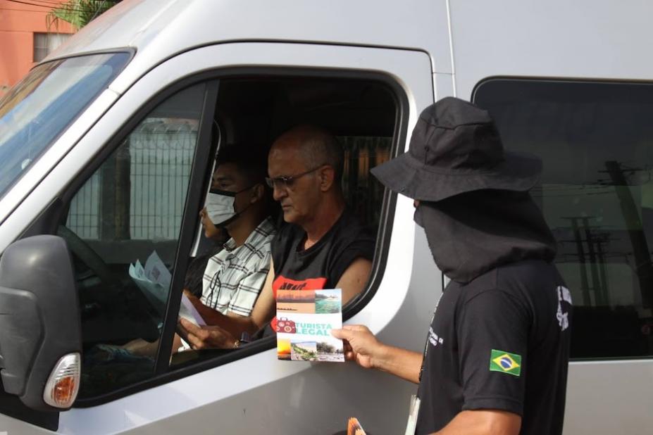 Agente entrega panfleto informativo para motorista dentro de veículo. #pracegover