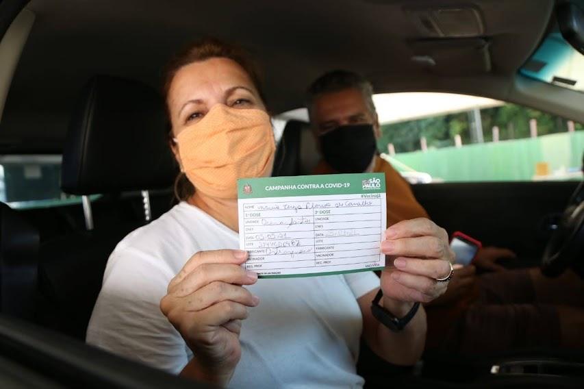 mulher dentro de carro sorri segurando comprovante de vacinação. #paratodosverem