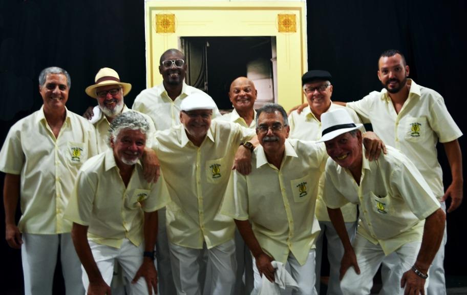 Integrantes da roda de samba ouro verde posam para foto. Todos usam camisa amarela e calça branca. #paratodosverem