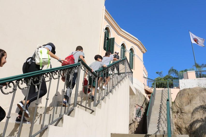 crianças sobem escada externa do Outeiro de Santa  Catarina. ao fundo e ao lado direito, num pedestal, tremula a bandeira de santos sob o céu azul. #paratodosverem