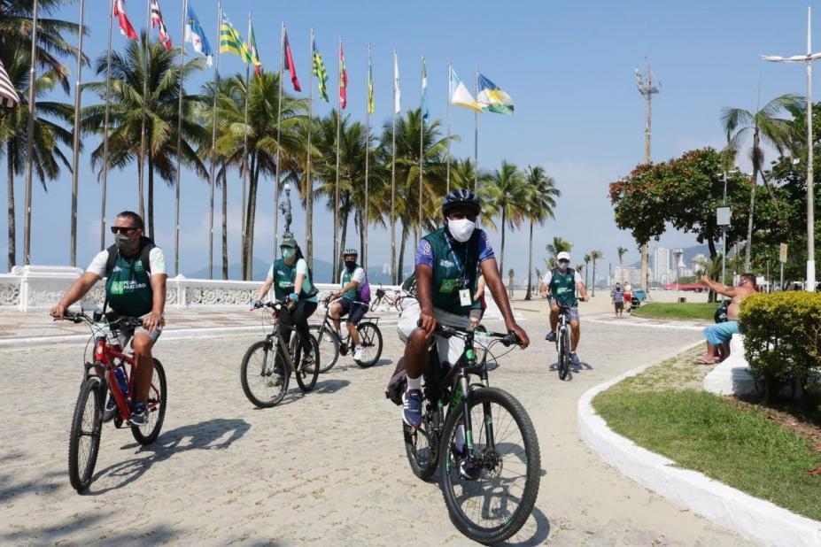 ciclisctas então sobre as bikes, usando máscaras, na orla, cruzando a Praça das Bandeiras. #paratodosverem