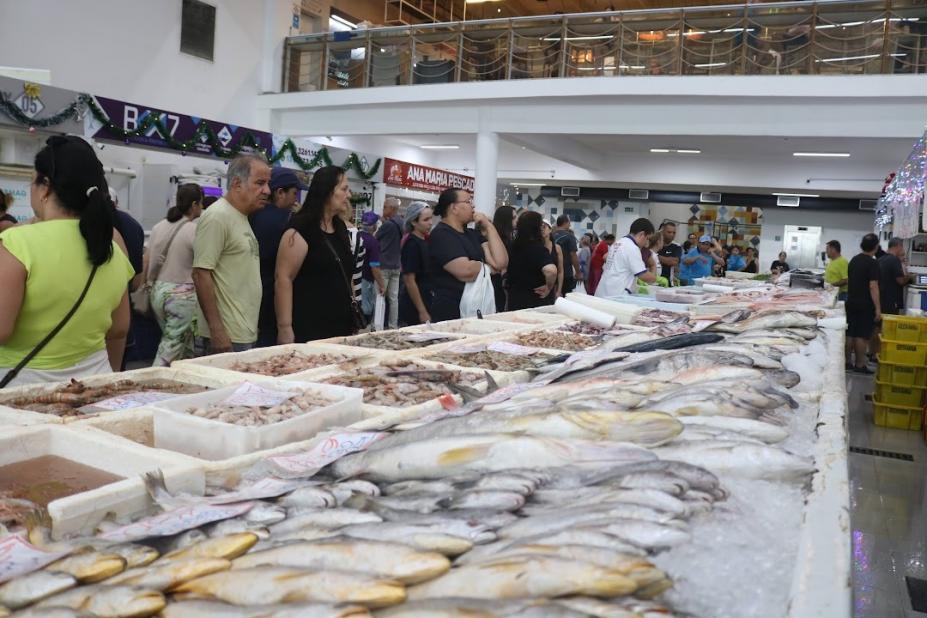 pessoas olham peixes expostos no mercado #paratodosverem 